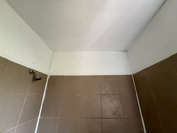 Original brown tile tub surround with the old shower arm still in place, before the room was taken back