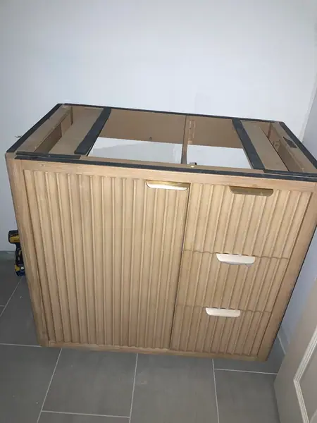 A fluted wood vanity set in place, waiting on its top.