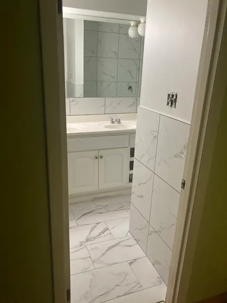 Finished bathroom seen from the doorway: marble-look floor and wall tile, a double vanity and a full-width mirror