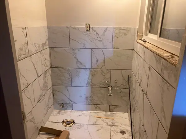 A walk-in shower tiled out in marble-look porcelain, the valve stubbed and the pan set.