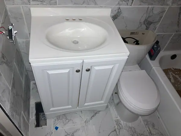 A new vanity and toilet set against marble-look porcelain carried up the wall and across the floor.