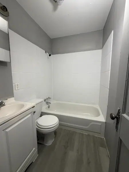 Compact bathroom finished in white tile and grey paint, with a new vanity, toilet and plank floor