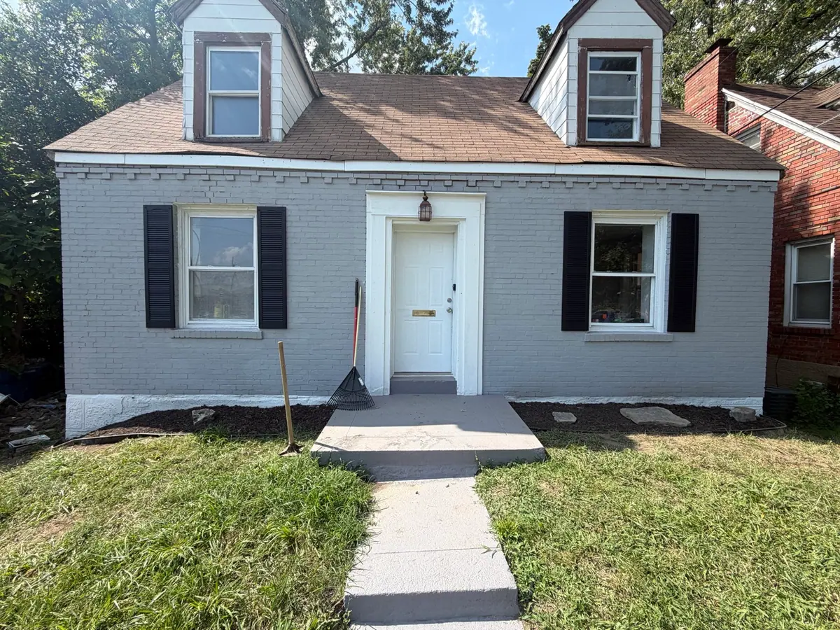 The same cape after: brick painted soft grey, black shutters hung, a new lamp over the door, mulch beds cut in either side and the walk cleared