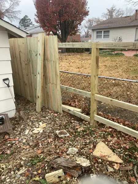 A cedar privacy panel set where a split-rail run ends, posts in and the ground still under leaves.