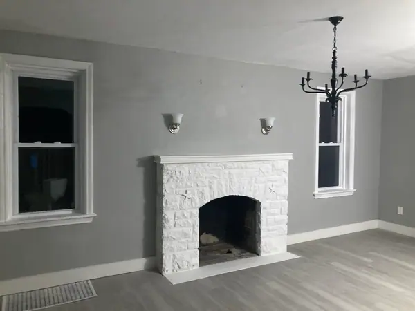The finished fireplace wall from the dining side, with sconces either side of the mantel and a black chandelier hung in the next room