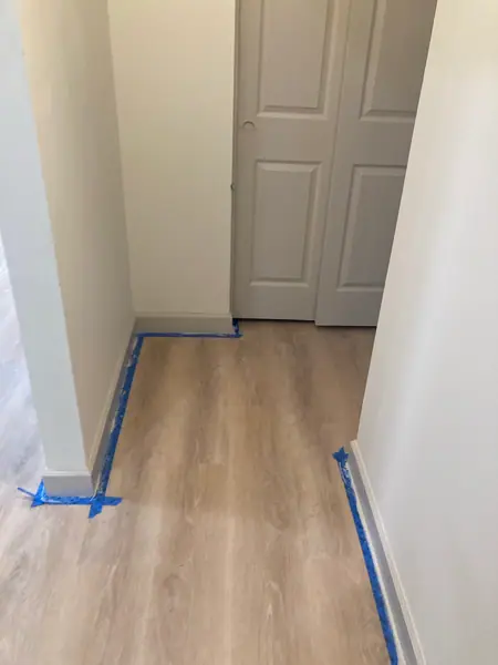 Hallway flooring run through to the next room, baseboards taped off for paint.