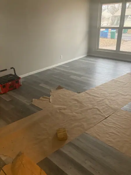 Plank flooring going down across a living room, laid out over the underlayment with the tools still on the floor.