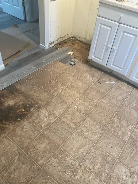 The old ceramic tile floor coming up beside the cabinets, with the new flooring started at the doorway.