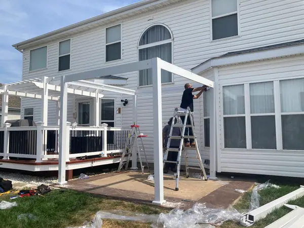 A white pergola going up over a rear deck, one of the crew working off a ladder.