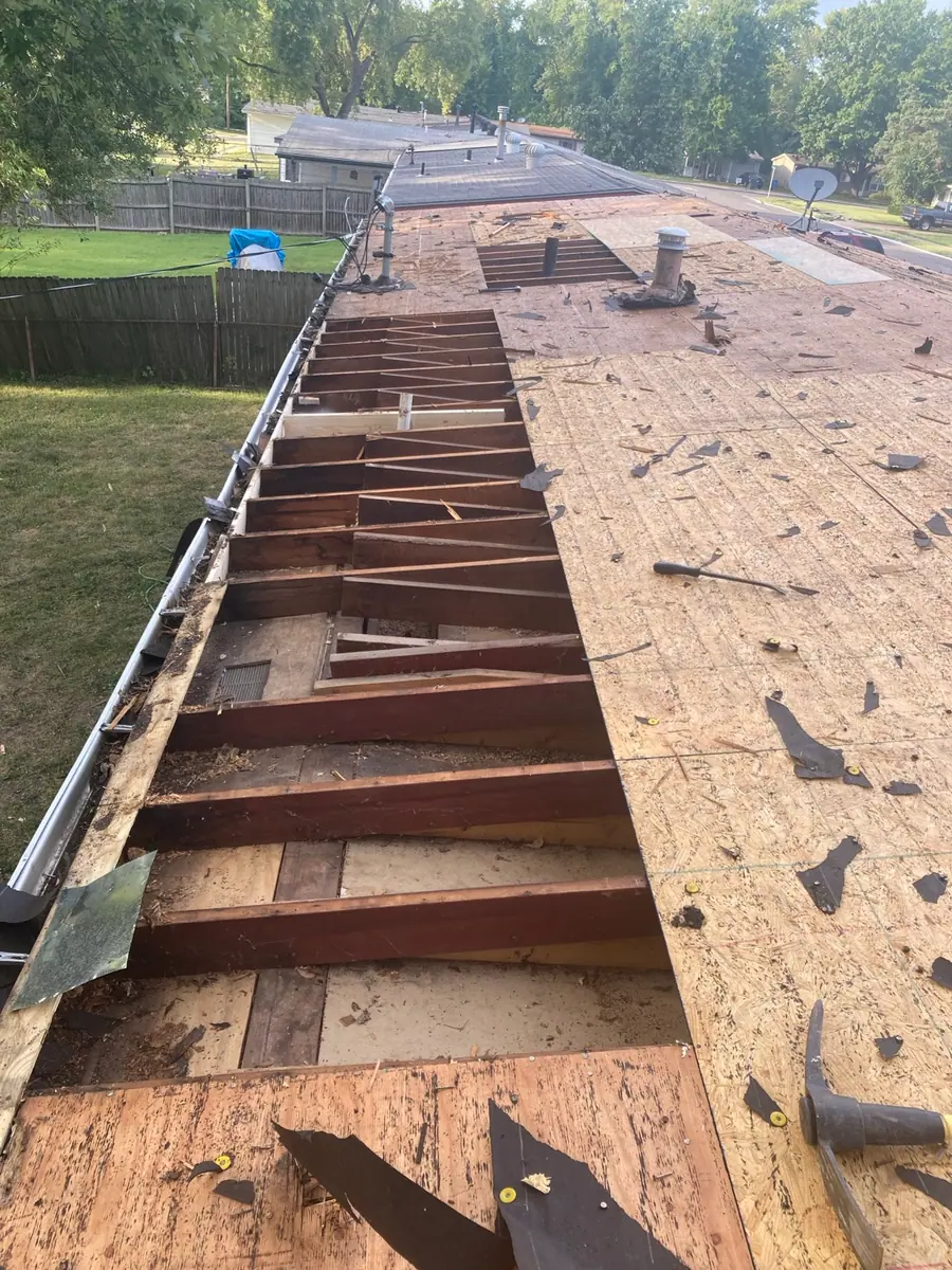 Roof stripped to the deck along the eave, with rotten boards out and the rafters and framing open to the air