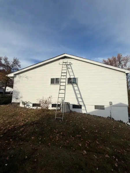 A ladder set against the gable end of a white-sided house, with the ground along the foundation freshly turned.