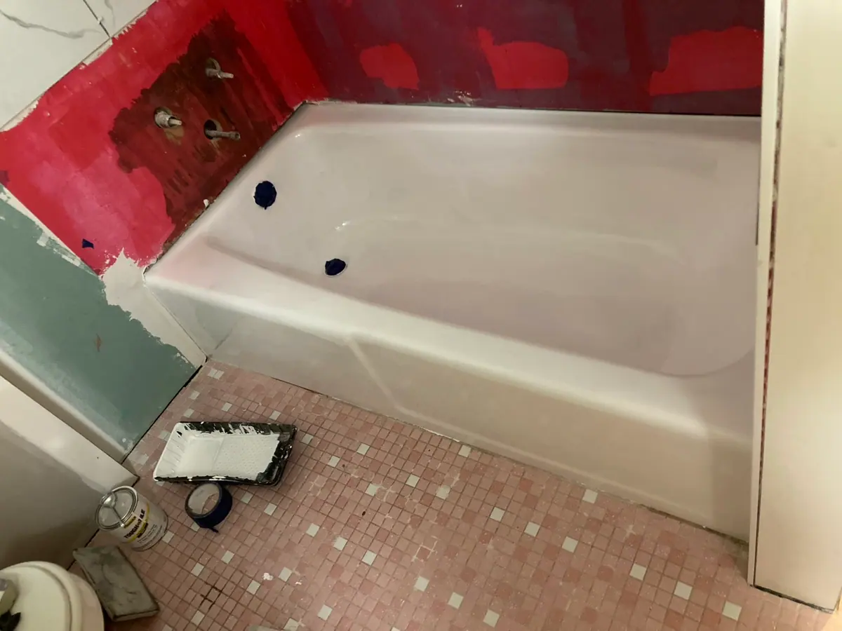 The same tub refinished in white, drain and overflow still masked off, taken from the same corner of the room