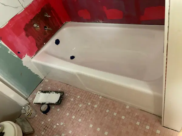 The same tub refinished in white, drain and overflow still masked off, taken from the same corner of the room